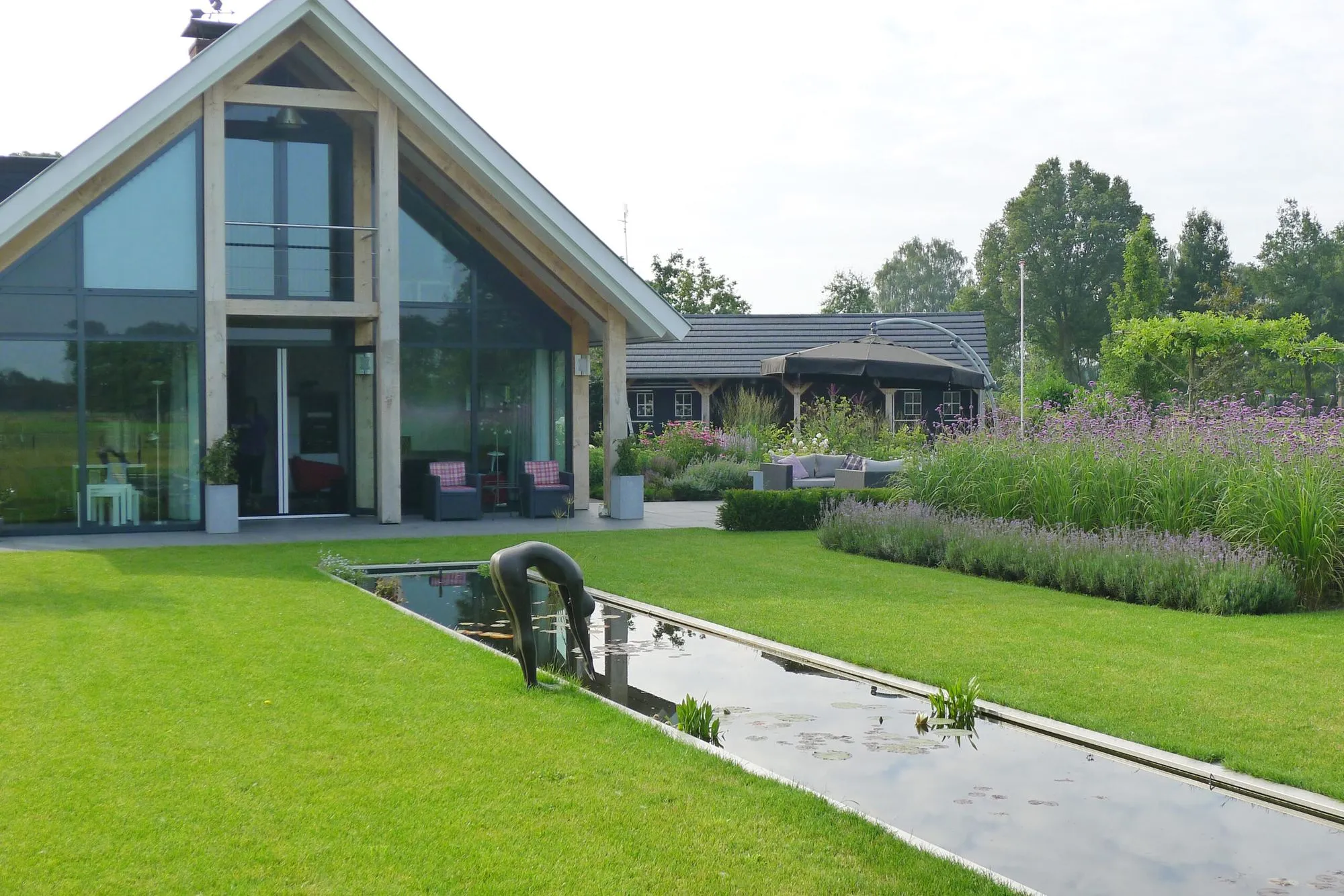 Weelderige border met lavendel en Verbena langs een gazon met zicht op een houten bijgebouw